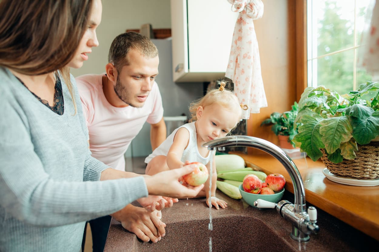 Young Couple With Daughter Washing Fruit