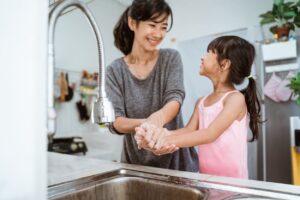 Mother And Daughter Washing Hands In Kitchen