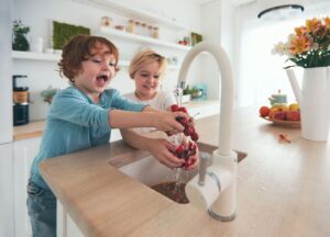 Two Young Kids Using Clean Water At Kitchen Faucet
