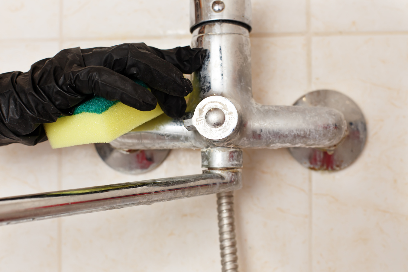 Limescale crust on bathroom mixer faucet. Hands in disposable ru